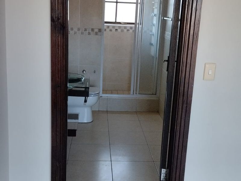 A view into a functional bathroom featuring a shower enclosure, toilet, and neutral wall and floor tiling with dark timber door trim.