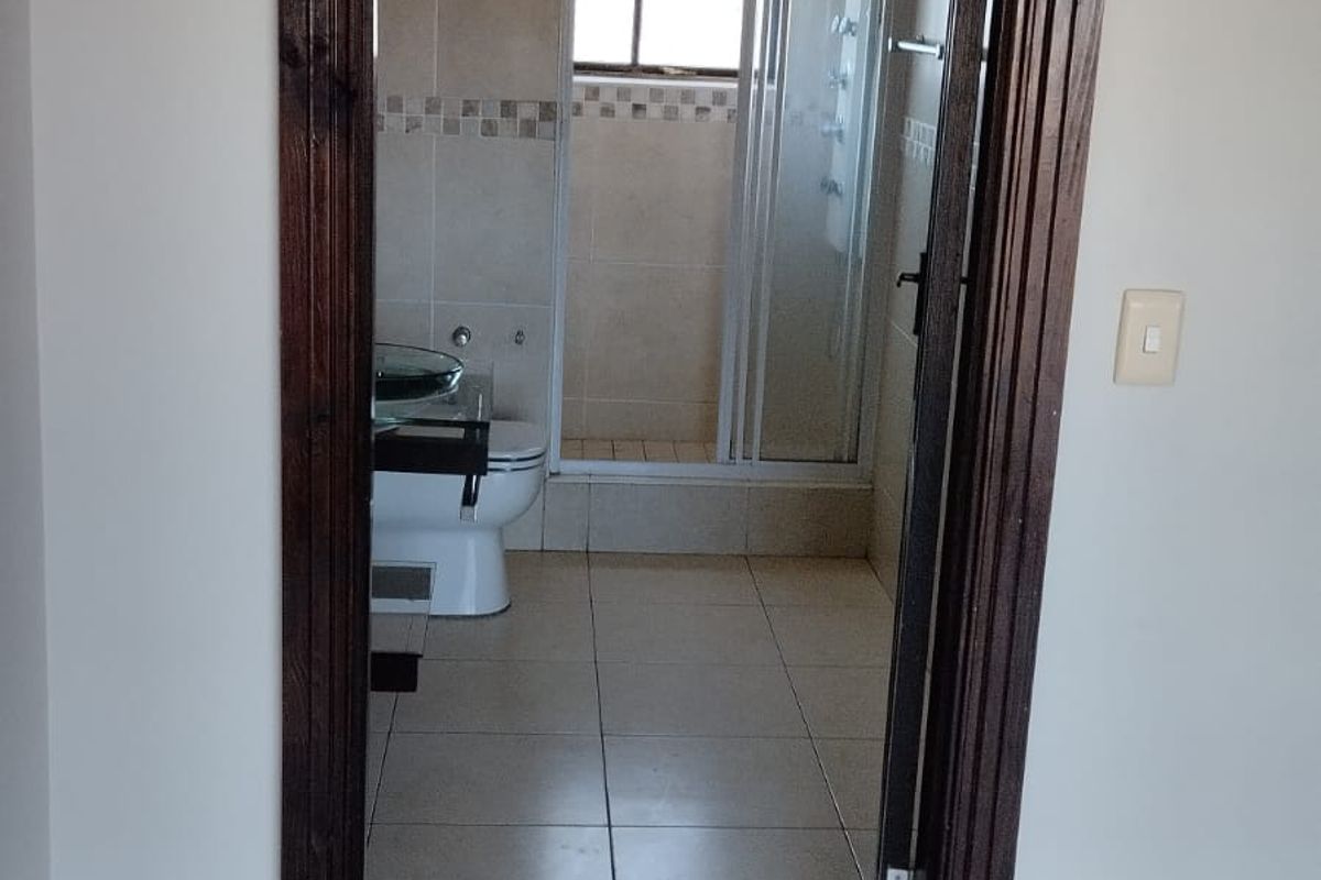 A view into a functional bathroom featuring a shower enclosure, toilet, and neutral wall and floor tiling with dark timber door trim.