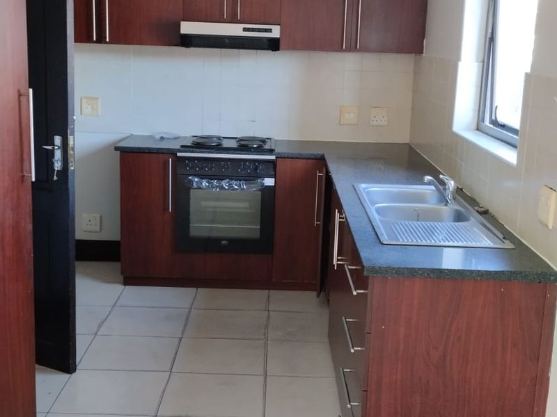 Functional kitchen featuring dark wood-look cabinetry, granite countertops, built-in oven with hob, and a stainless steel double sink with tiled splashback.