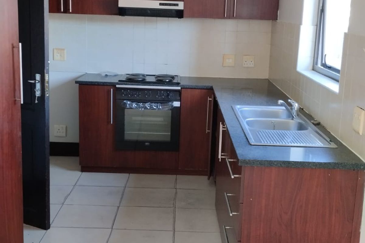 Functional kitchen featuring dark wood-look cabinetry, granite countertops, built-in oven with hob, and a stainless steel double sink with tiled splashback.