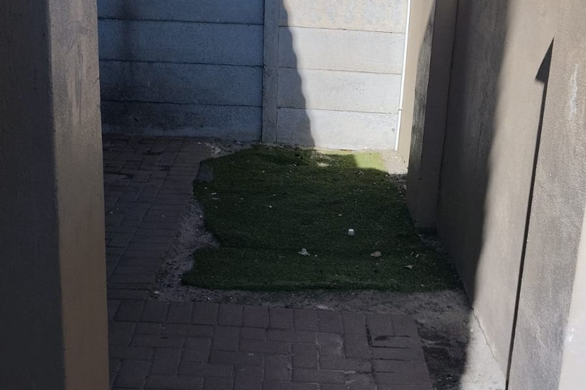 A small rear courtyard area featuring paved flooring, a precast concrete boundary wall, and a patch of artificial grass.