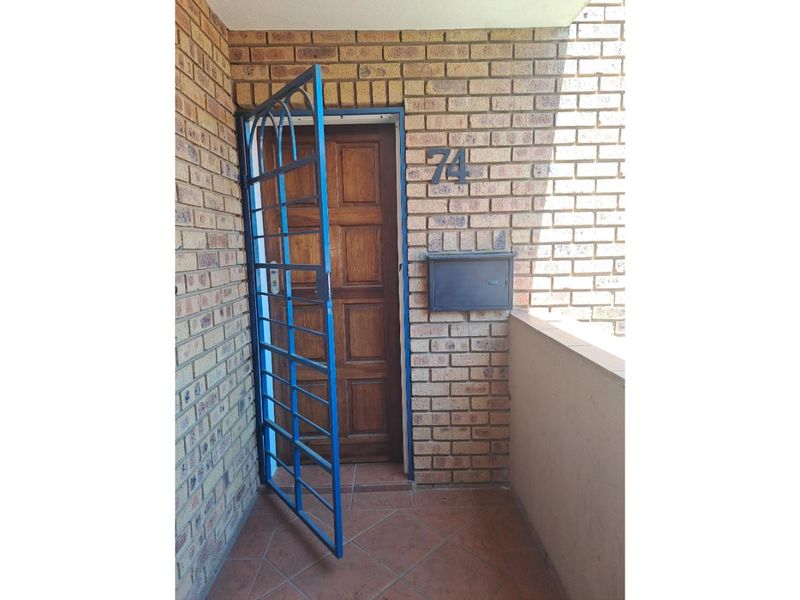 Entrance area featuring a brick facade, a wooden front door with a blue security gate, and a wall-mounted mailbox.