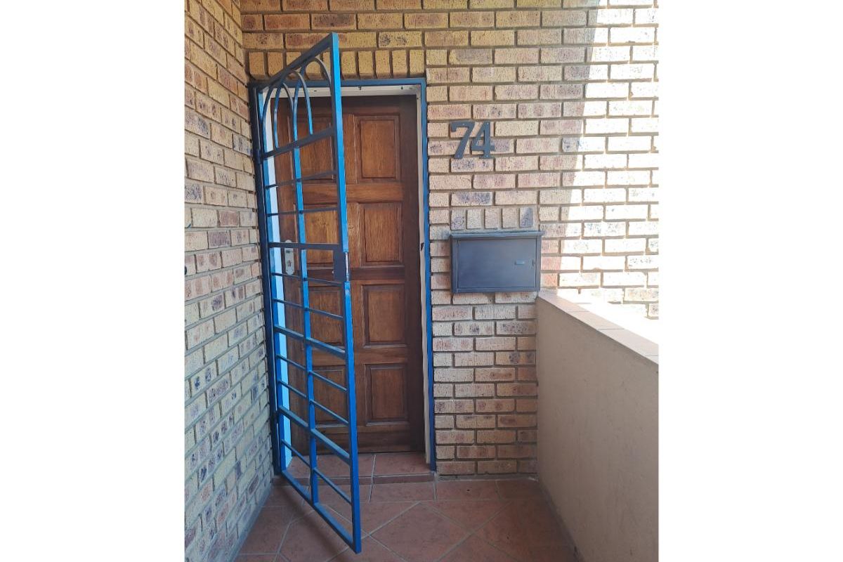 Entrance area featuring a brick facade, a wooden front door with a blue security gate, and a wall-mounted mailbox.