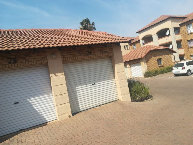 Exterior view of a residential apartment complex featuring multiple secure roll-up garage units with tiled roofing and paved driveway access.