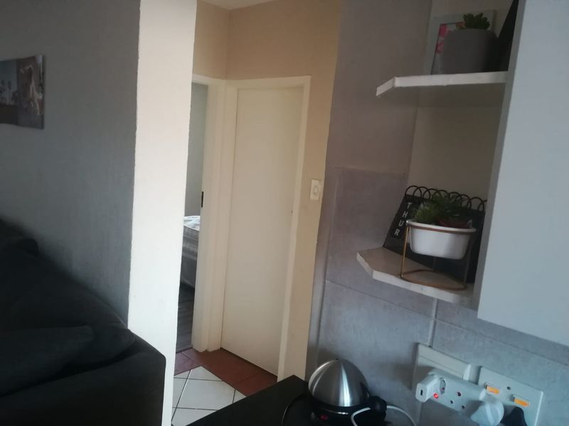 A view of a kitchen area featuring built-in shelving and tiled splashbacks, with a doorway leading to an adjacent bedroom.