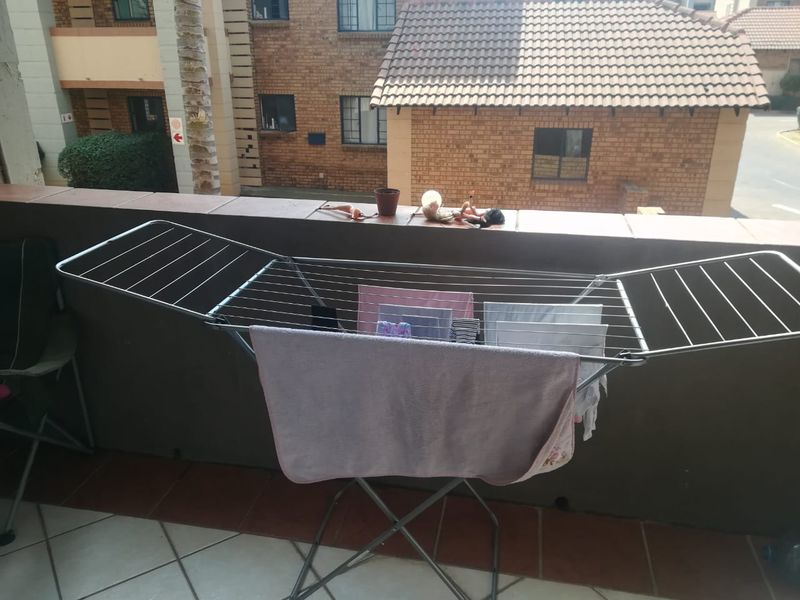 A functional balcony space featuring tiled flooring and a brick parapet wall, overlooking the apartment complex grounds.