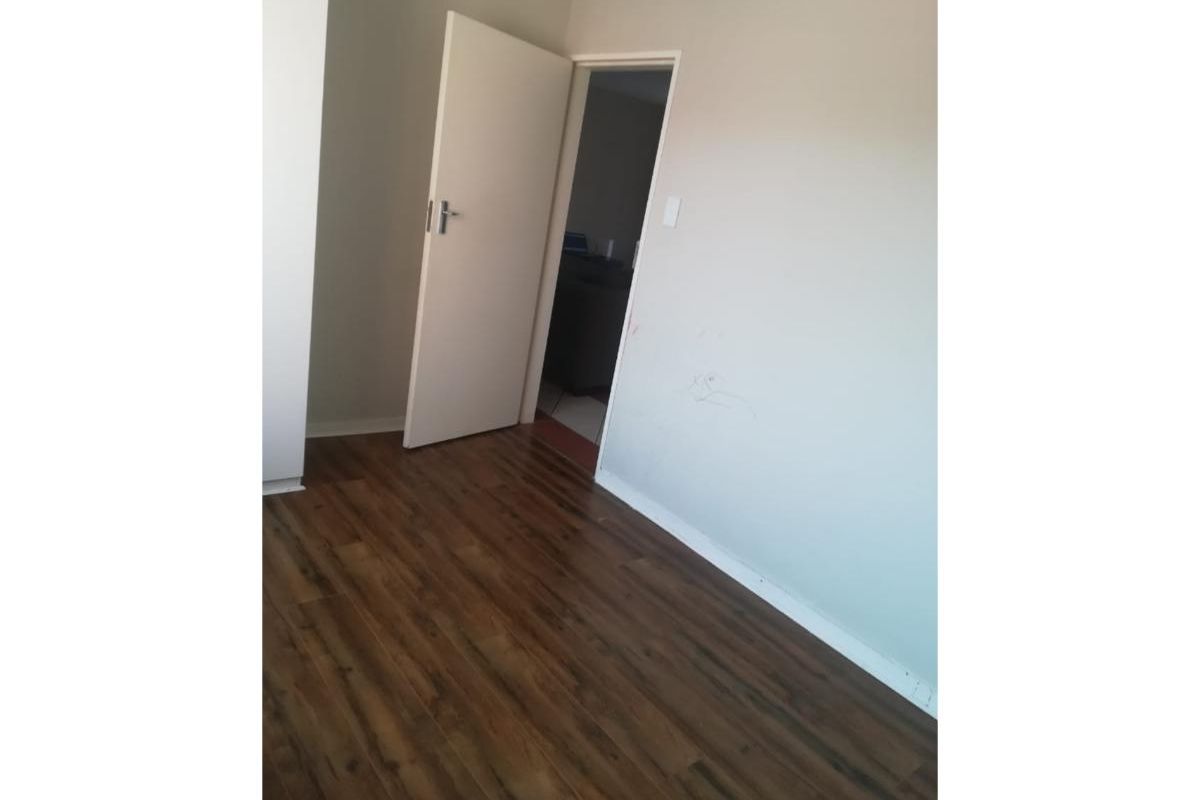 An empty bedroom featuring dark laminate flooring and neutral wall finishes, ready for personalization.