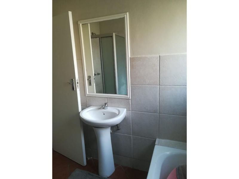 A functional bathroom featuring a pedestal basin, wall-mounted mirror, shower enclosure, and bathtub with neutral wall tiling.