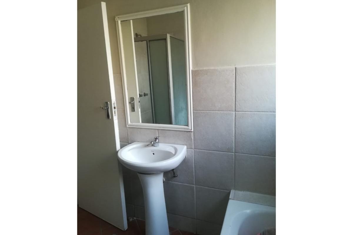 A functional bathroom featuring a pedestal basin, wall-mounted mirror, shower enclosure, and bathtub with neutral wall tiling.