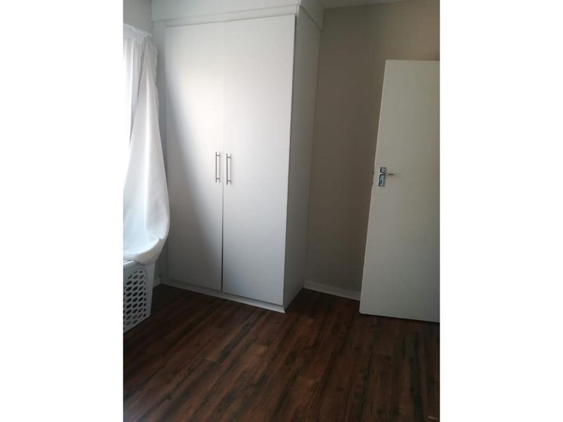 A clean, empty bedroom featuring modern laminate flooring and a white built-in wardrobe, offering a neutral space ready for personalization.