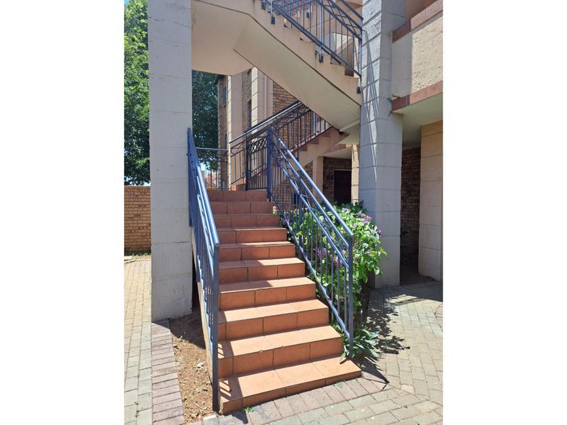 Exterior view of an apartment complex entrance featuring a tiled staircase with metal balustrades and concrete structural pillars.