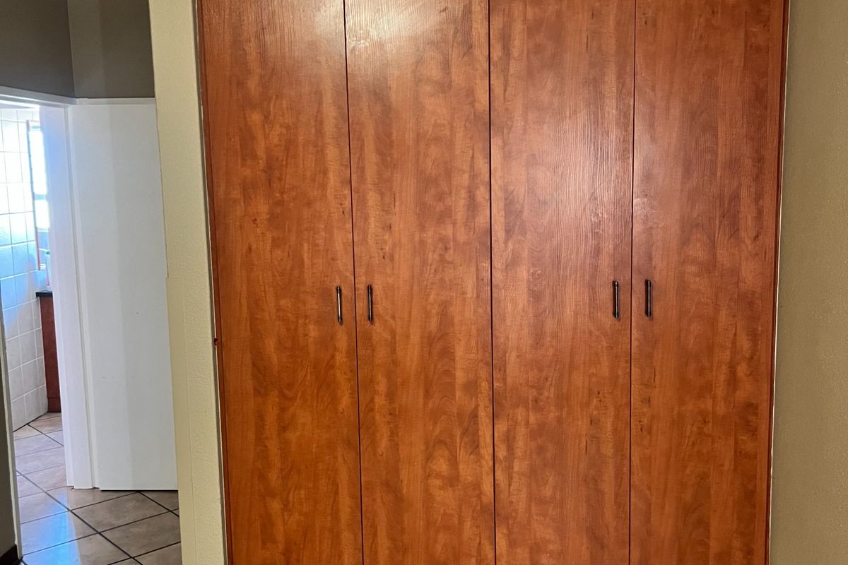 A bedroom featuring built-in wooden cupboards with a tiled floor, providing ample storage space.