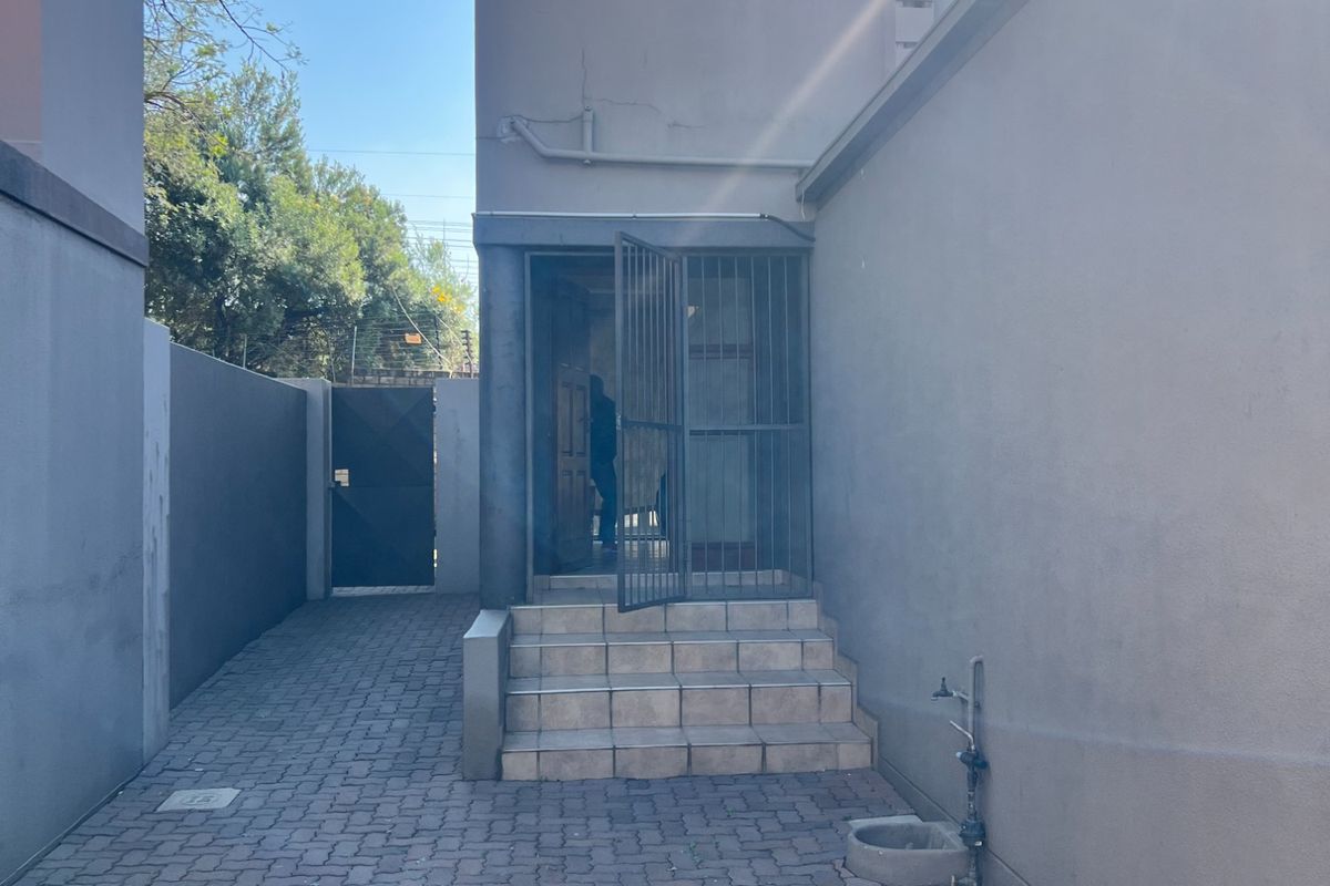 A view of the rear exterior area featuring paved ground, concrete steps leading to the entrance, and a security gate.