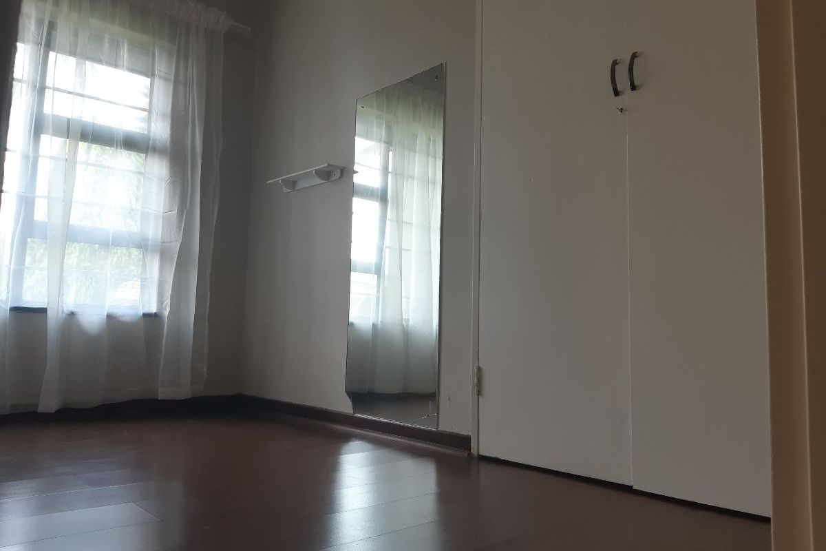 A bright, empty bedroom featuring laminate flooring and built-in cupboards, offering a clean and neutral space ready for personalization.