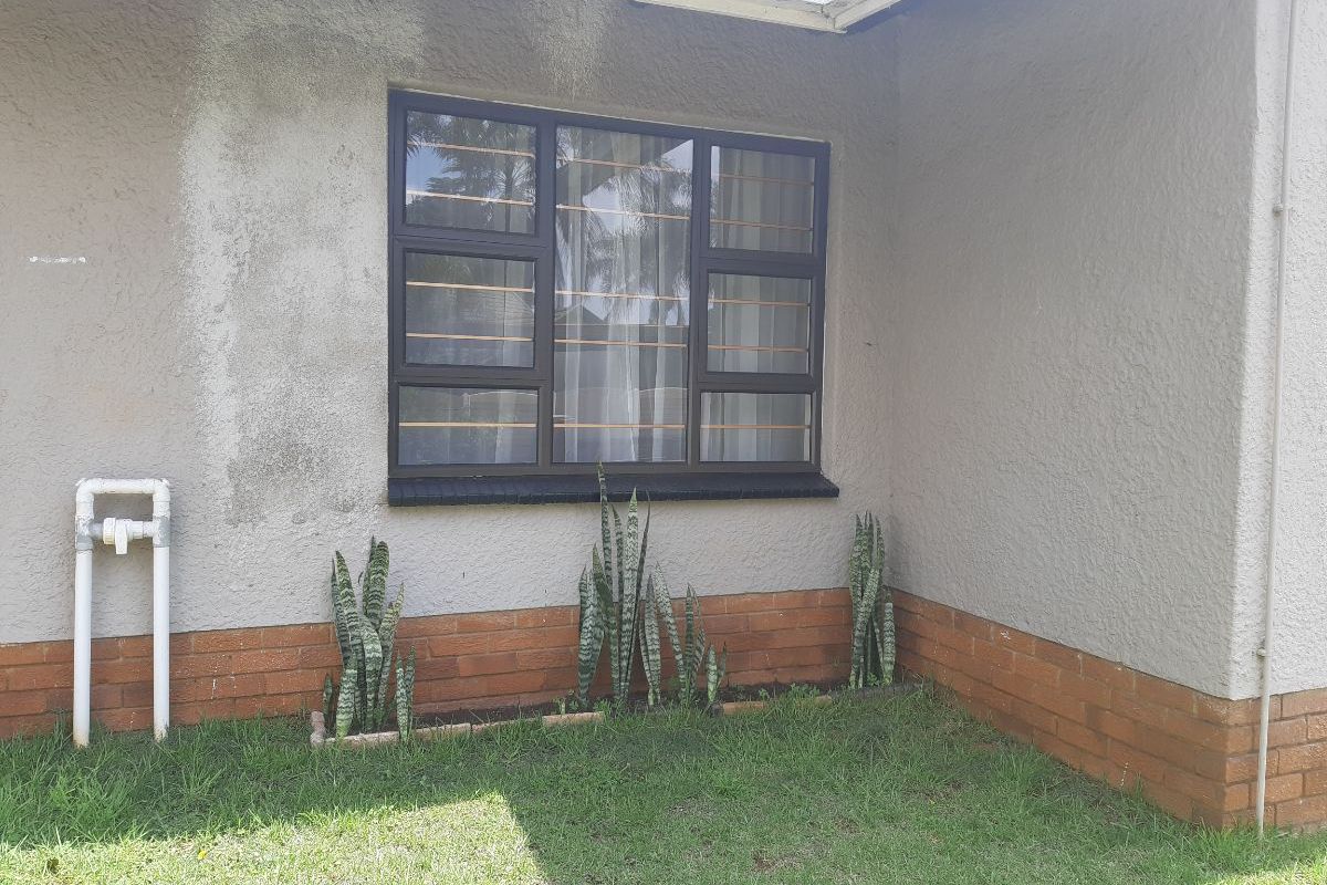 A view of the cottage exterior featuring a window with security bars, brick base detailing, and visible wall staining requiring maintenance.