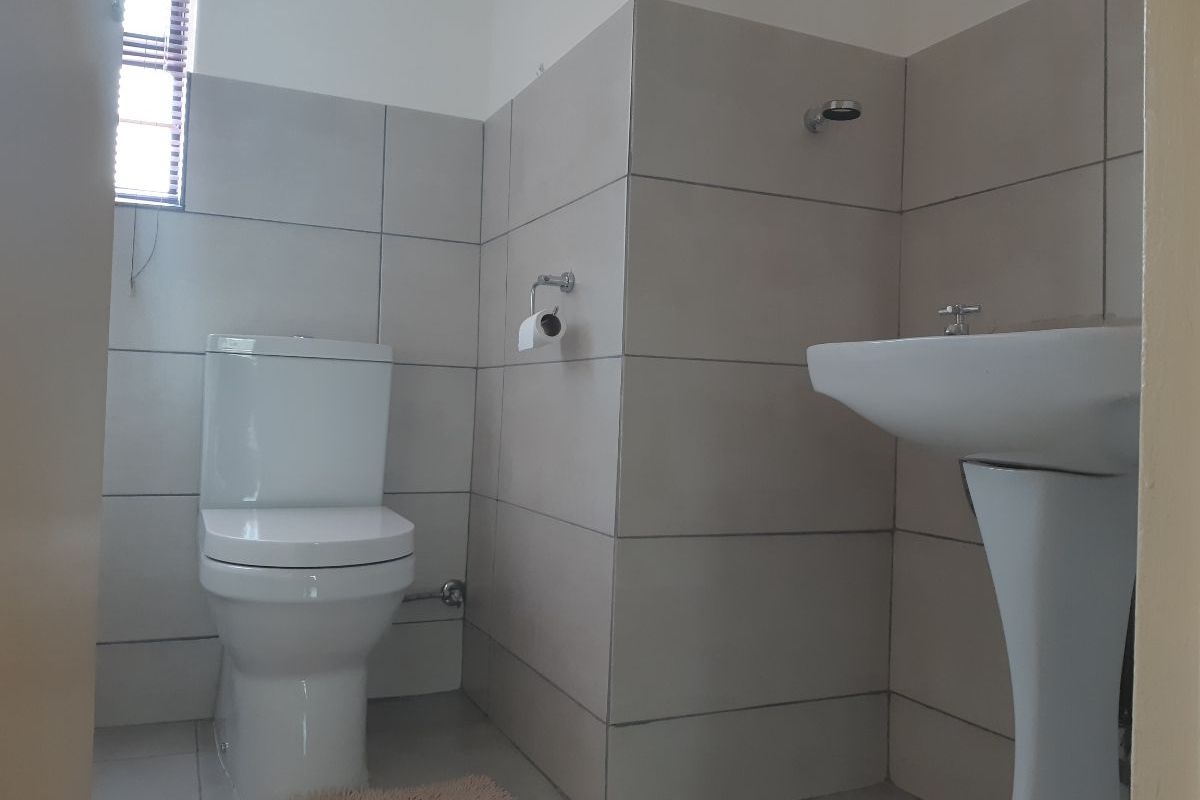 A clean, modern bathroom featuring neutral wall tiles, a pedestal basin, and a standard toilet.