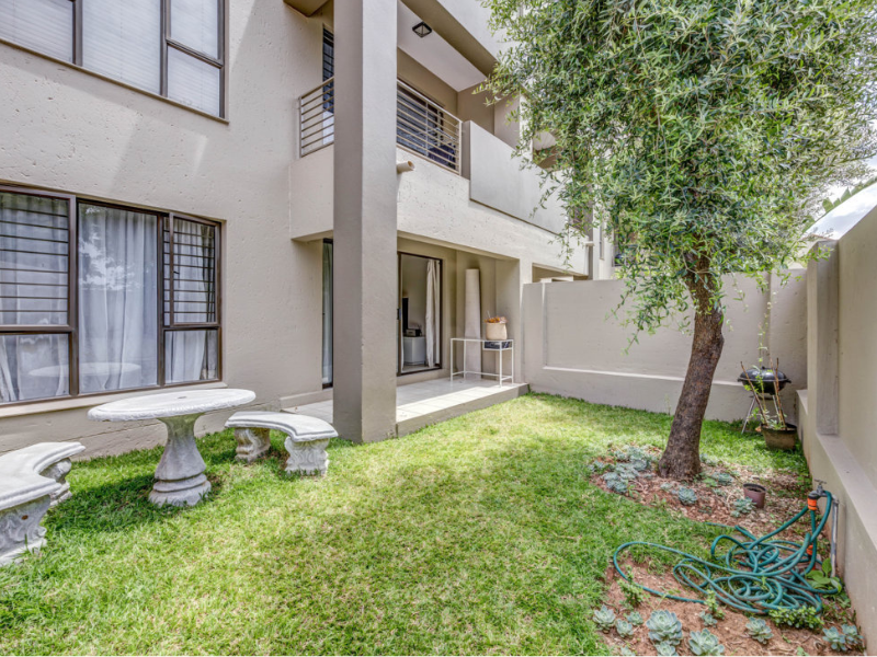 A private rear garden area featuring a covered patio, lawn, mature tree, and secure boundary walls, providing a pleasant outdoor space.