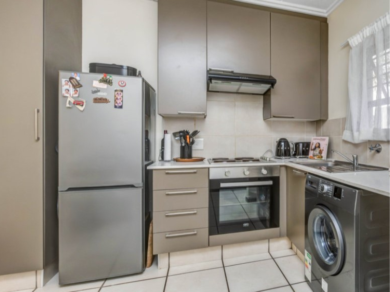 Compact kitchen featuring modern taupe cabinetry, built-in oven and hob, extractor fan, and tiled flooring with a functional layout.