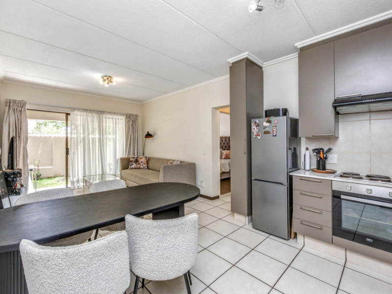 Open-plan living and kitchen area featuring tiled flooring, modern cabinetry, built-in oven and hob, and direct access to an outdoor patio through sliding doors.