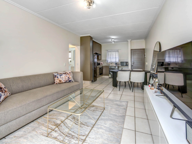 An open-plan living and kitchen area featuring tiled flooring, neutral walls, and a functional kitchen layout with built-in cabinetry and appliances.