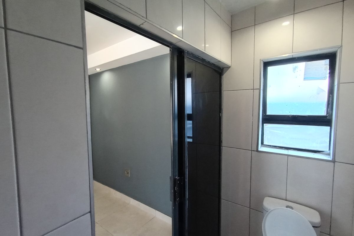 A modern bathroom featuring floor-to-ceiling wall tiles, a sliding door entrance, and a window, providing a clean and functional space.
