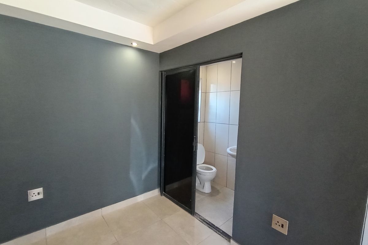 A bedroom featuring dark grey walls, tiled flooring, recessed ceiling lighting, and an en-suite bathroom with a toilet and basin.