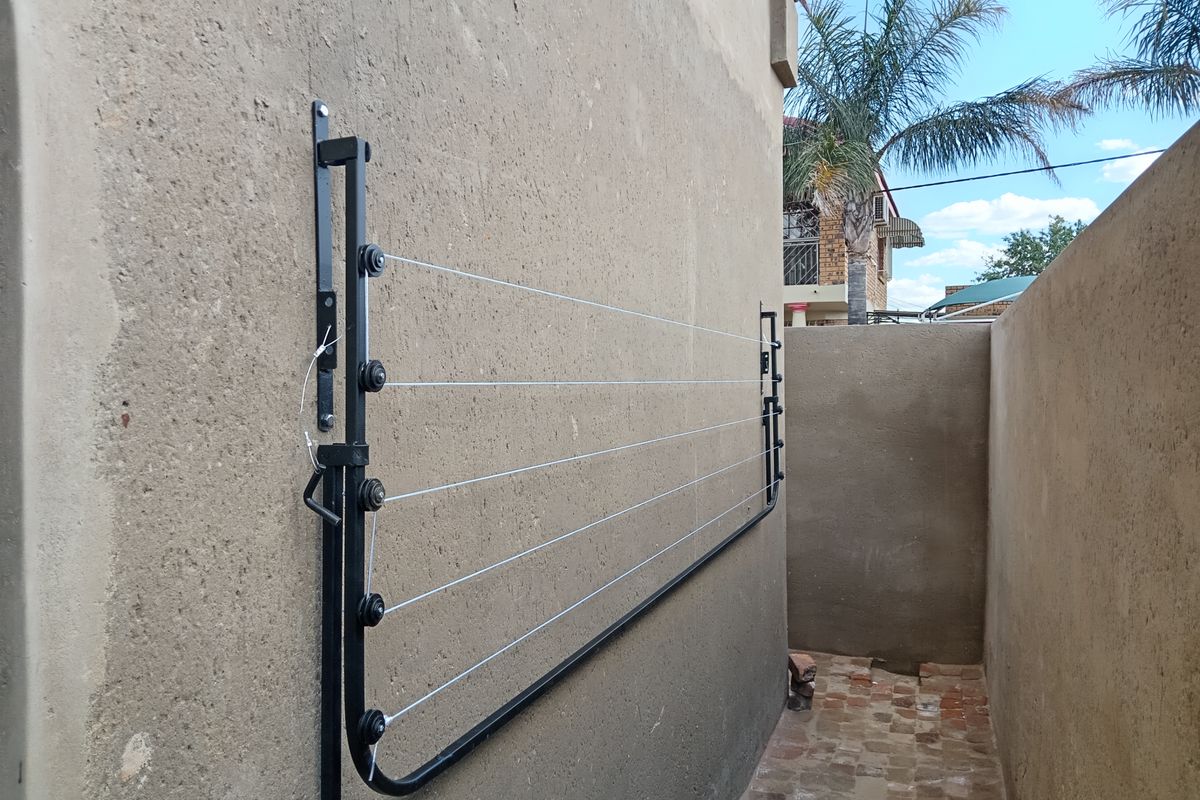 A side exterior area featuring a wall-mounted retractable clothesline and brick paved flooring.