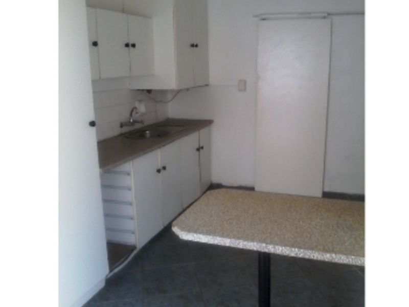 A compact, dated kitchen featuring basic white cabinetry, a laminate countertop, and tiled flooring, offering potential for a modern renovation.