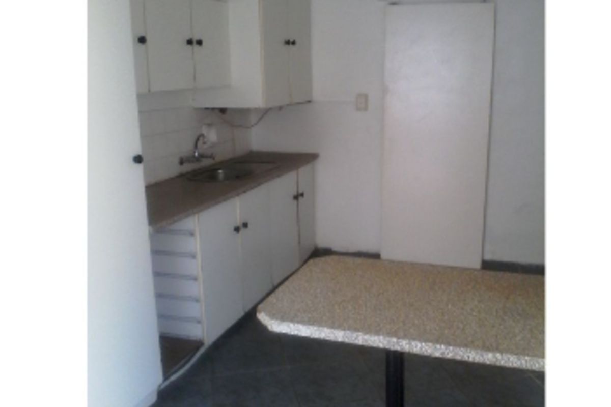 A compact, dated kitchen featuring basic white cabinetry, a laminate countertop, and tiled flooring, offering potential for a modern renovation.