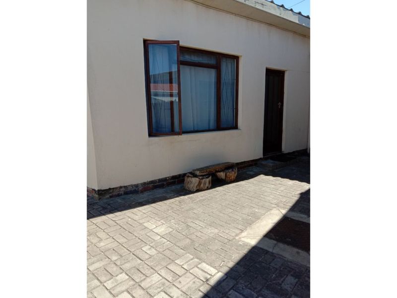 A rear exterior view of the cottage featuring a paved patio area, timber-framed window, and a secure entrance door.
