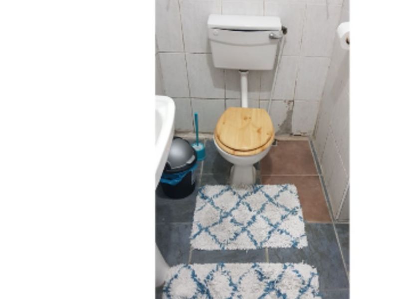 A compact bathroom featuring a pedestal basin and toilet with tiled walls and flooring, currently showing signs of wear and requiring maintenance.