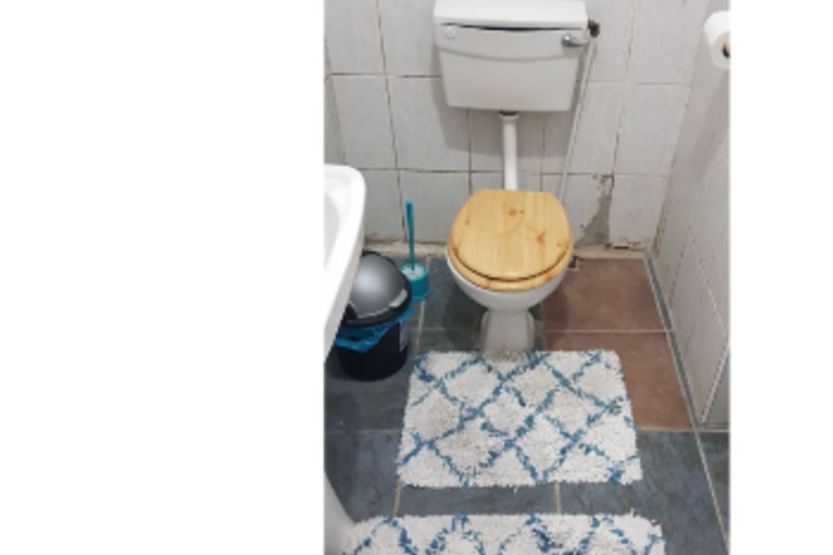 A compact bathroom featuring a pedestal basin and toilet with tiled walls and flooring, currently showing signs of wear and requiring maintenance.