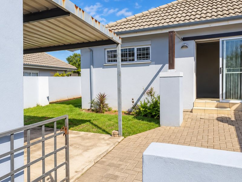 Rear exterior view of the townhouse featuring a paved patio area, a metal carport, and a small garden space with boundary walls.
