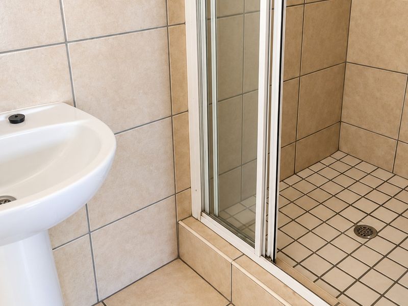 A functional bathroom featuring a pedestal basin with chrome mixer tap and a tiled shower enclosure with a sliding glass door.