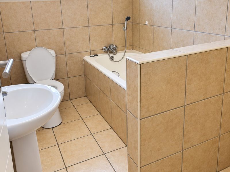 A functional bathroom featuring a pedestal basin, toilet, and a built-in bathtub with tiled surround and walls.