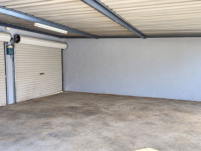 A spacious, empty garage featuring a roller door, metal roofing, and concrete flooring, providing secure parking or additional storage space.