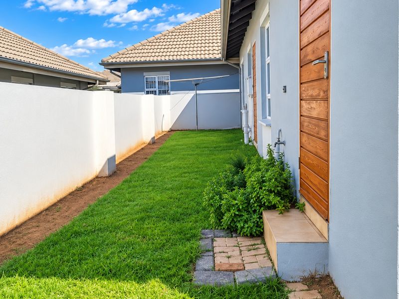 A well-maintained rear garden area featuring a neat lawn, boundary wall, and direct access to the property via a timber door.