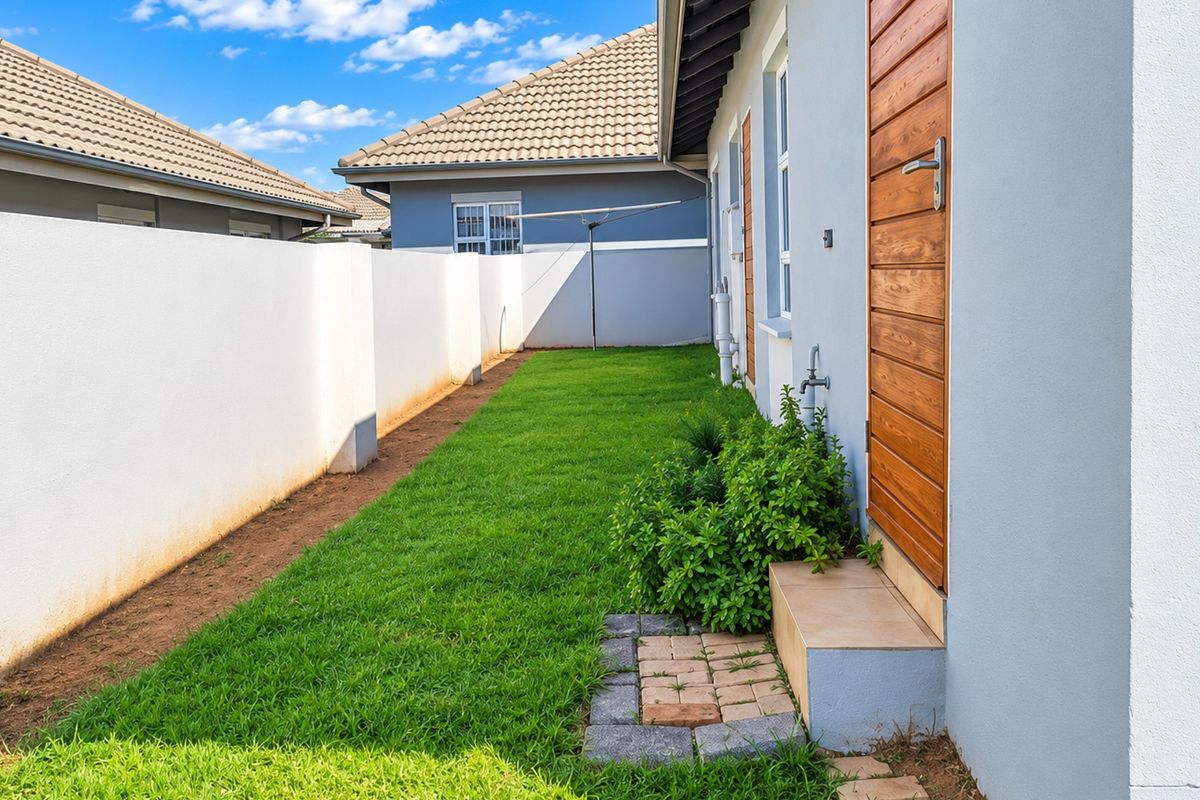A well-maintained rear garden area featuring a neat lawn, boundary wall, and direct access to the property via a timber door.