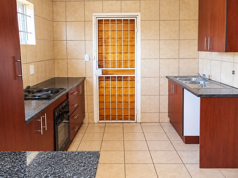 A functional kitchen featuring dark wood cabinetry, granite countertops, built-in oven and hob, and tiled finishes throughout, providing a clean and practical workspace.