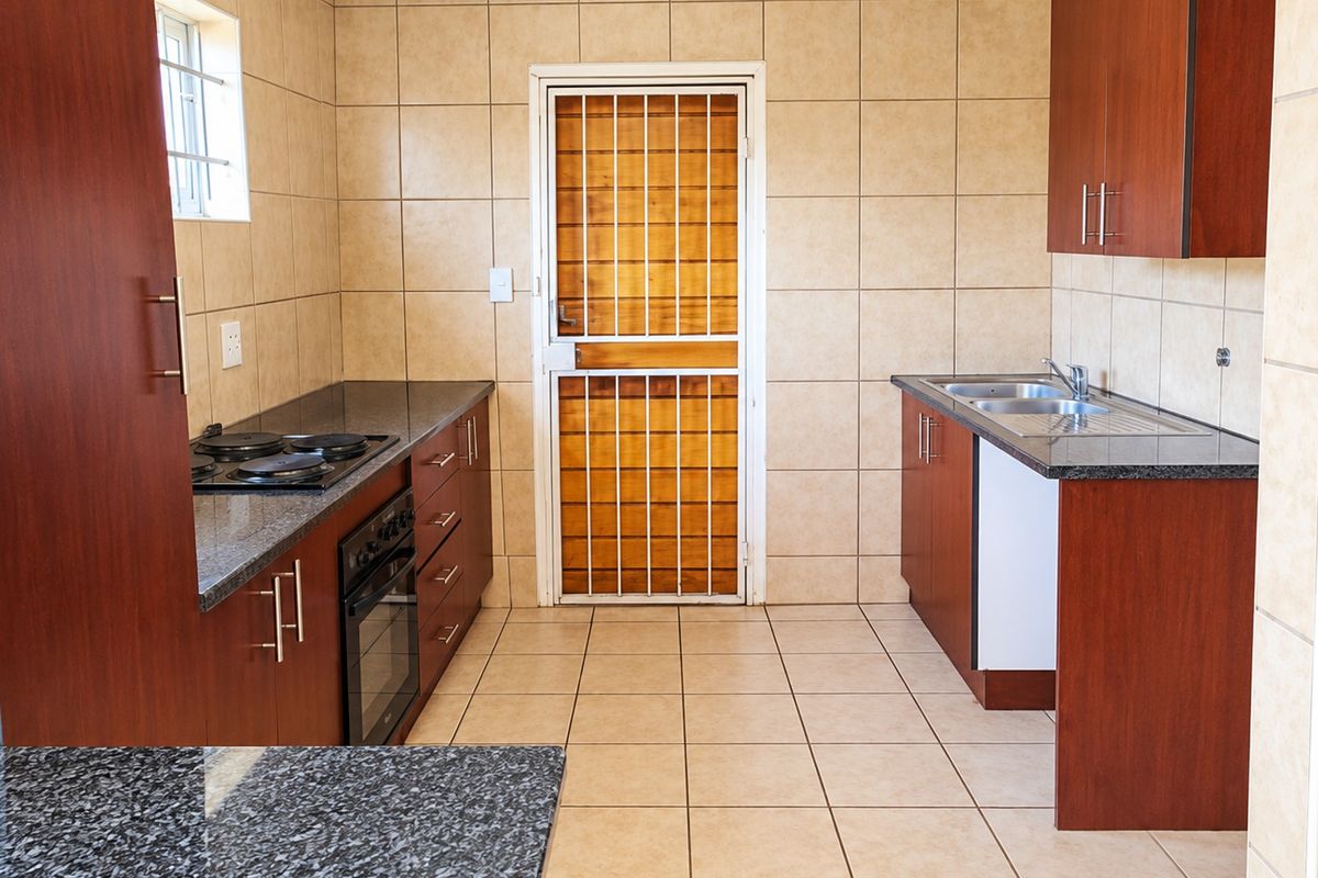 A functional kitchen featuring dark wood cabinetry, granite countertops, built-in oven and hob, and tiled finishes throughout, providing a clean and practical workspace.