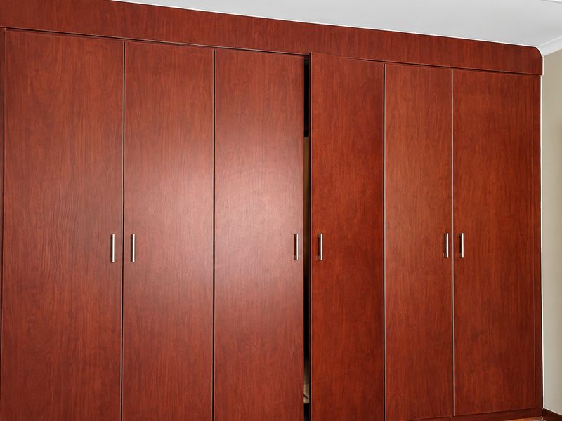 A bedroom featuring floor-to-ceiling built-in wooden cupboards with modern handles and a neutral interior door.