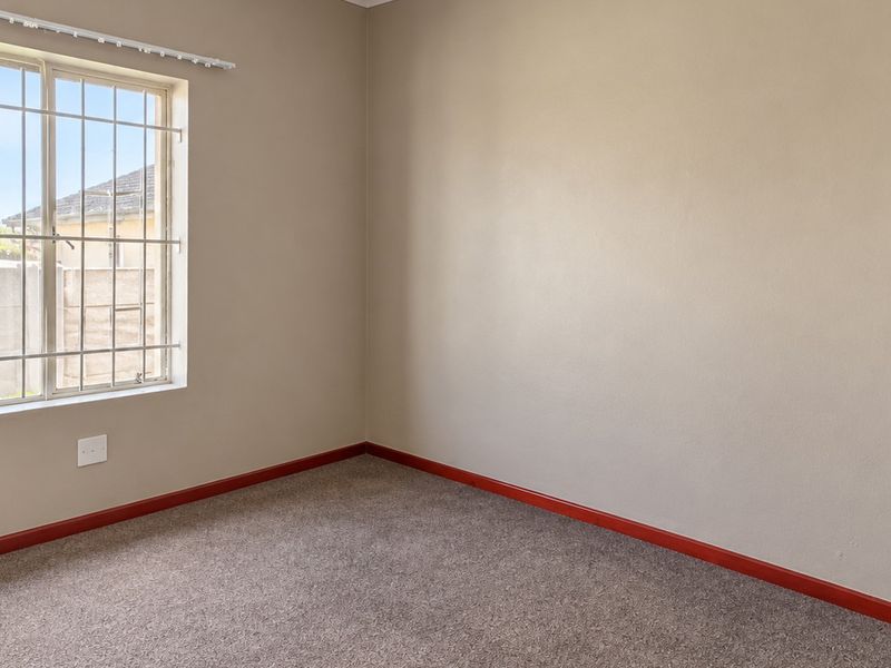An empty bedroom featuring neutral wall paint, carpeted flooring, and a window fitted with security bars.