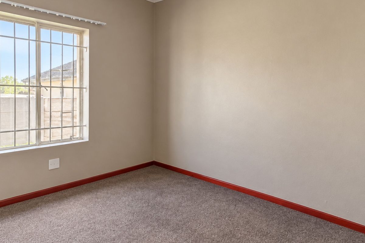 An empty bedroom featuring neutral wall paint, carpeted flooring, and a window fitted with security bars.