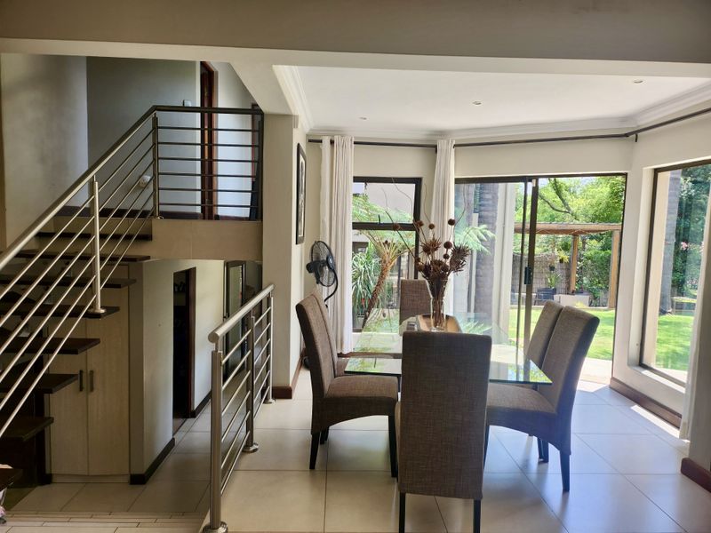 Bright open-plan dining area featuring tiled floors, modern stainless steel staircase railings, and large sliding glass doors providing seamless access to the rear garden.