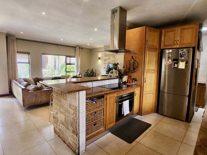 Open-plan kitchen and living area featuring a stone-clad breakfast bar, granite countertops, built-in oven, and warm wooden cabinetry with tiled flooring throughout.