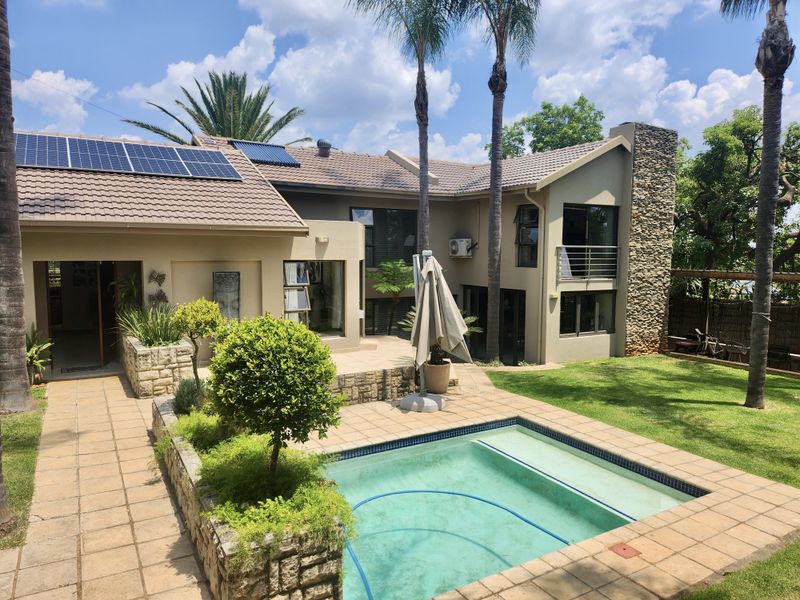 Rear exterior view featuring a swimming pool, paved patio area, stone-clad chimney, balcony, and roof-mounted solar panels.