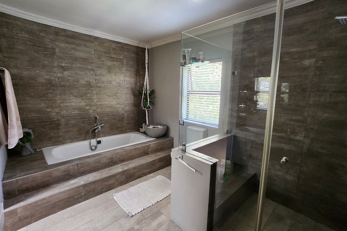 Modern bathroom featuring a raised built-in bathtub, a spacious glass-enclosed shower, and contemporary wood-look tile finishes throughout.