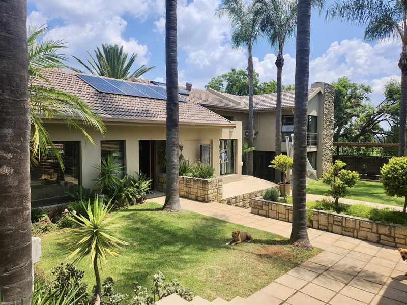 A well-maintained rear exterior view featuring a landscaped garden, paved patio areas, stone-clad accents, and roof-mounted solar panels.