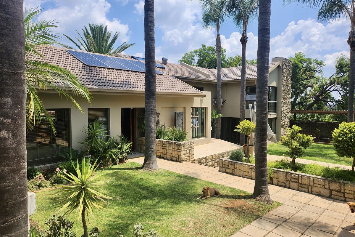 A well-maintained rear exterior view featuring a landscaped garden, paved patio areas, stone-clad accents, and roof-mounted solar panels.