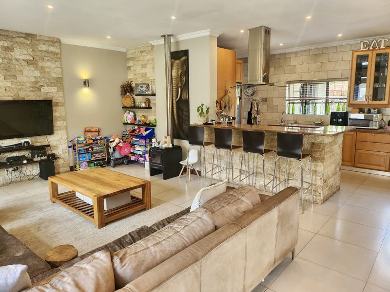 Spacious open-plan living area featuring a stone-clad fireplace wall, a functional kitchen with granite island, and modern tiled flooring throughout.